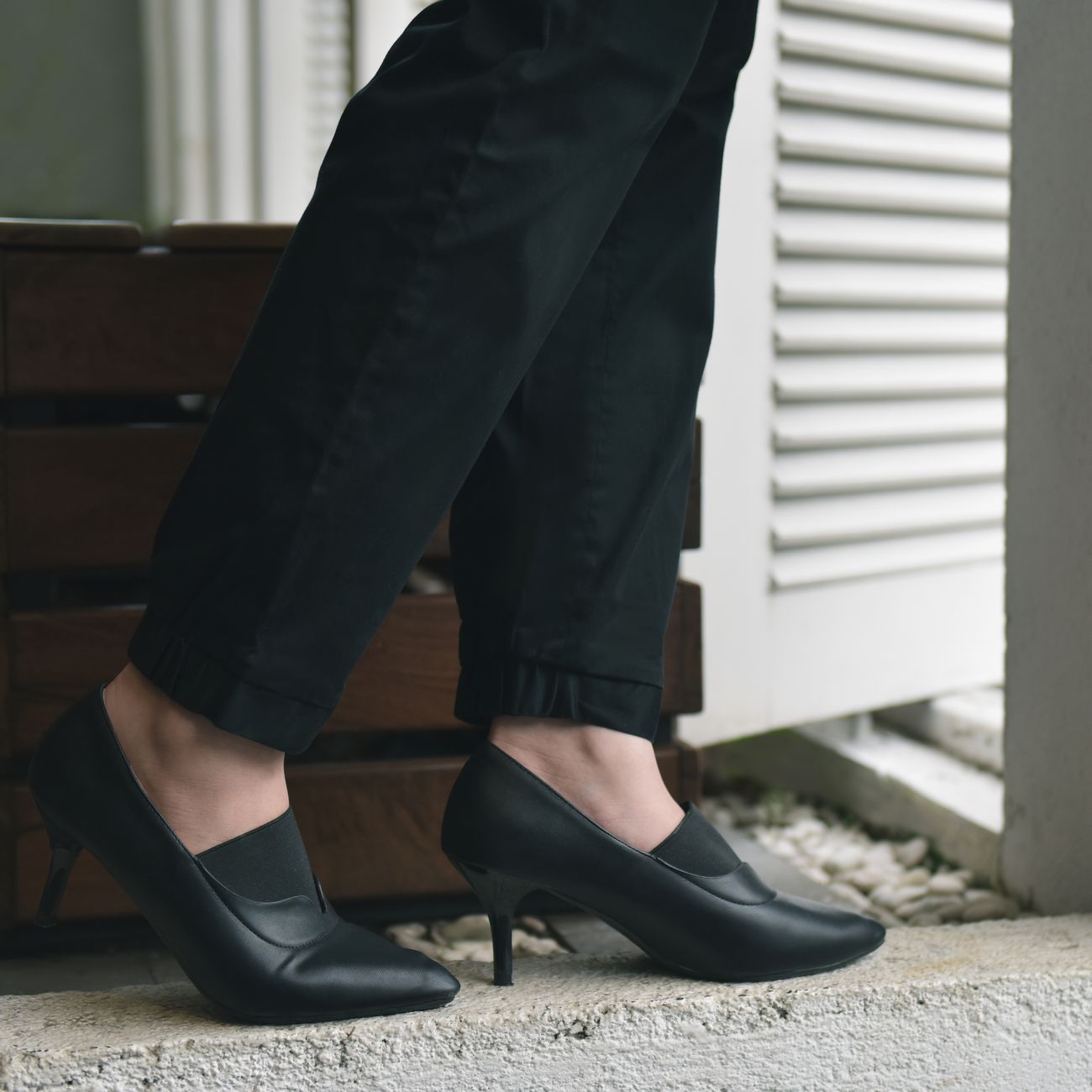 Close-up of elegant black heeled shoes paired with black trousers.
